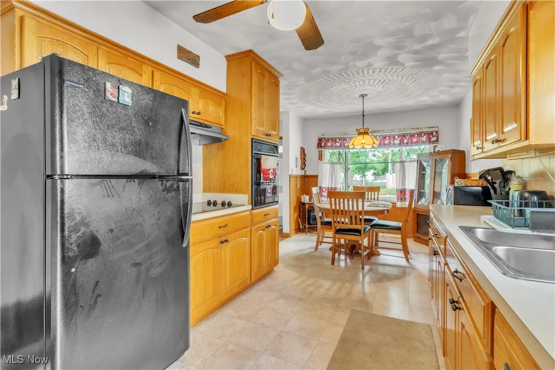 Kitchen with black appliances, ceiling fan, light countertops, range hood, and decorative light fixtures