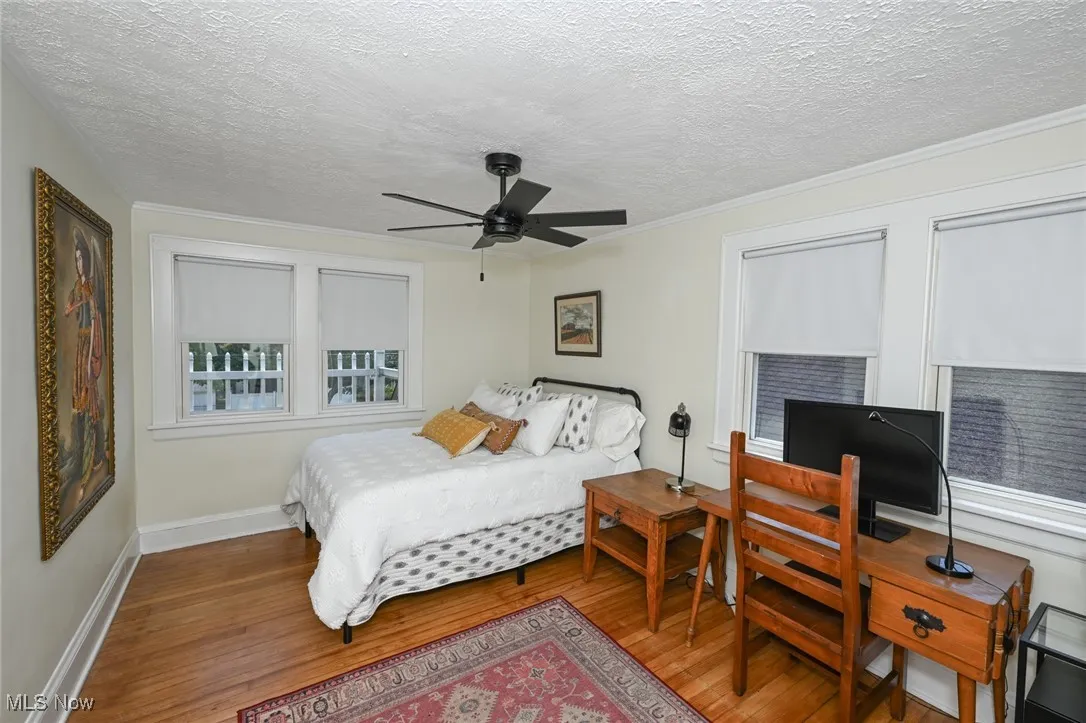 Bedroom featuring wood finished floors, a textured ceiling, ceiling fan, crown molding, and a desk