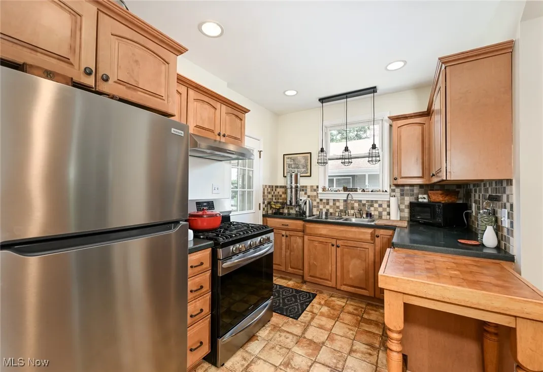 Kitchen with stainless steel appliances, under cabinet range hood, tasteful backsplash, decorative light fixtures, and light stone finish flooring