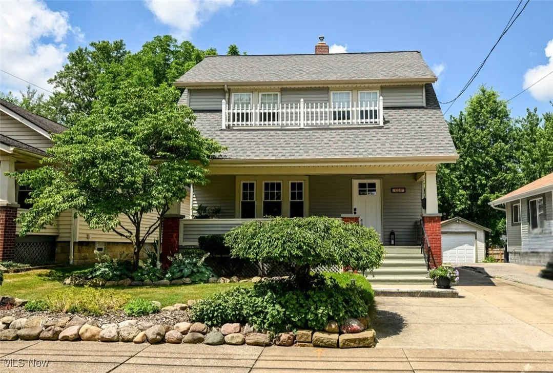 View of front facade featuring an outbuilding, a porch, a detached garage, a shingled roof, and a chimney