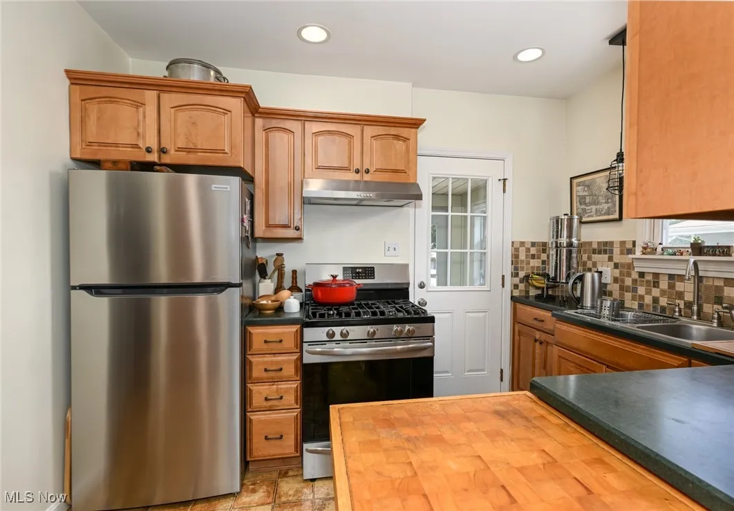 Kitchen featuring stainless steel appliances, under cabinet range hood, tasteful backsplash, brown cabinetry, and recessed lighting