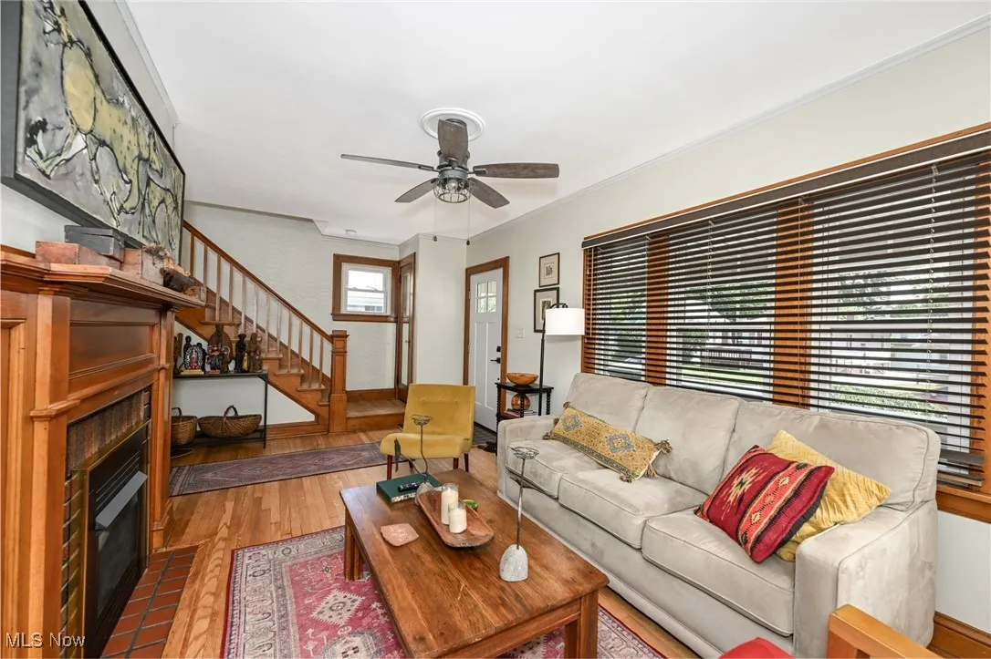Living area featuring a large fireplace, stairs, wood finished floors, and ceiling fan