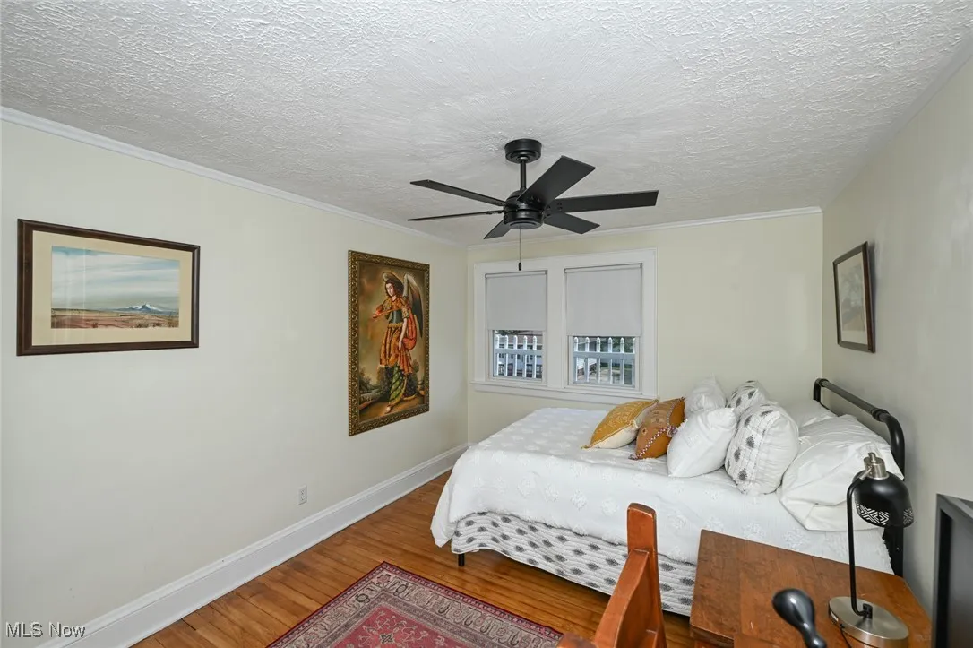 Bedroom featuring wood finished floors, a textured ceiling, a ceiling fan, and crown molding