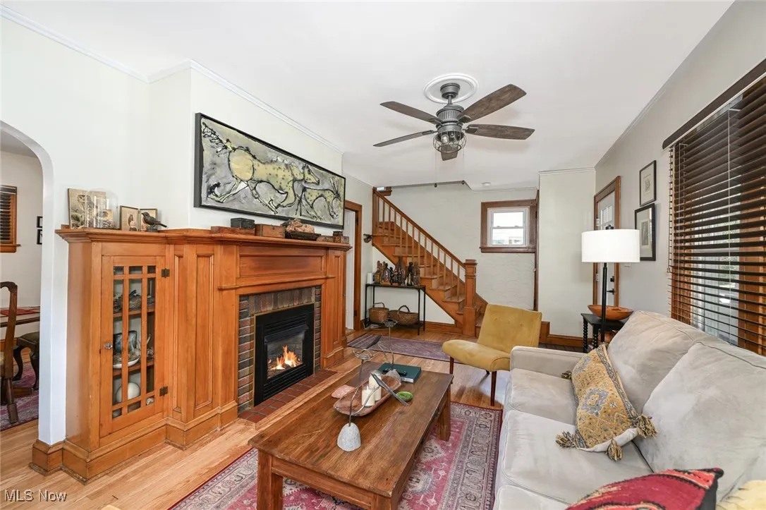 Living area with wood finished floors, a ceiling fan, a fireplace, arched walkways, and stairs