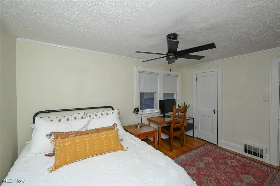 Bedroom featuring wood finished floors, crown molding, ceiling fan, and a textured ceiling