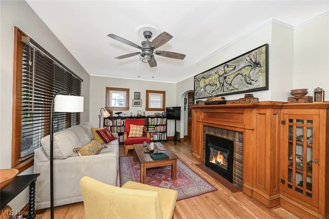 Living room with ceiling fan, crown molding, wood finished floors, arched walkways, and a fireplace