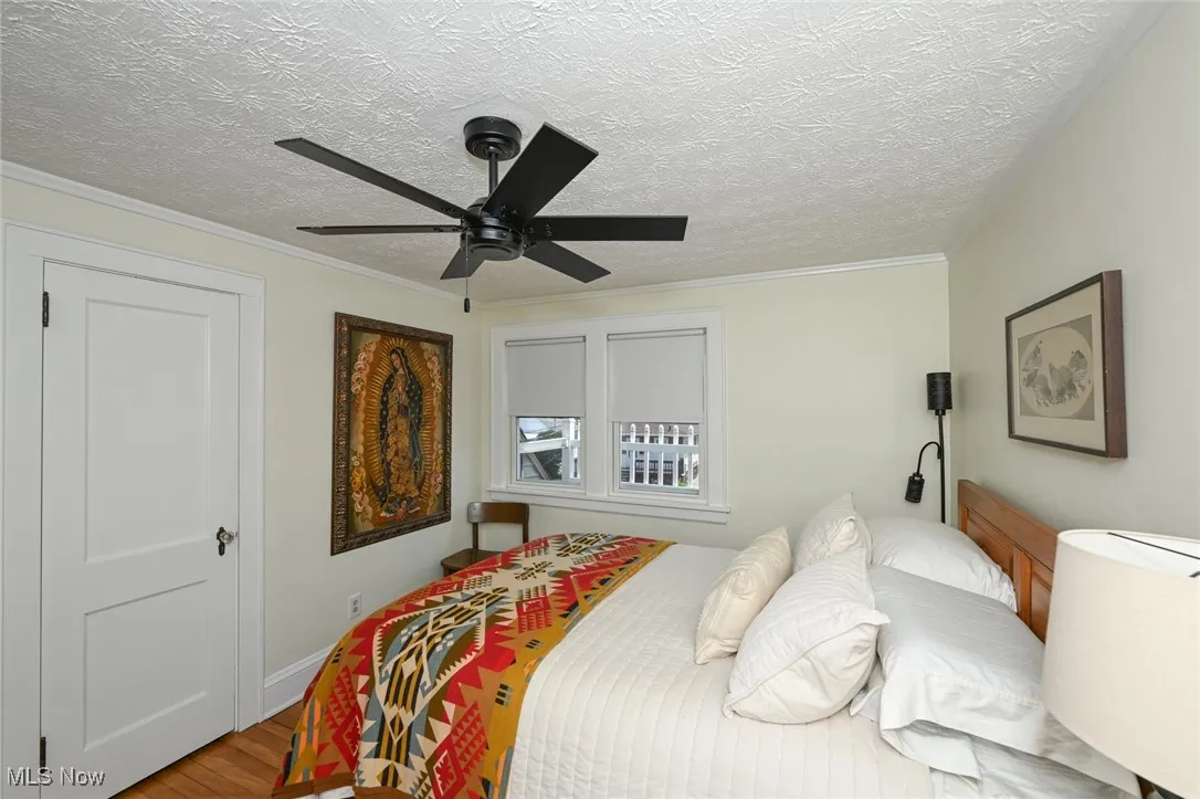 Bedroom with wood finished floors, a textured ceiling, a ceiling fan, and ornamental molding