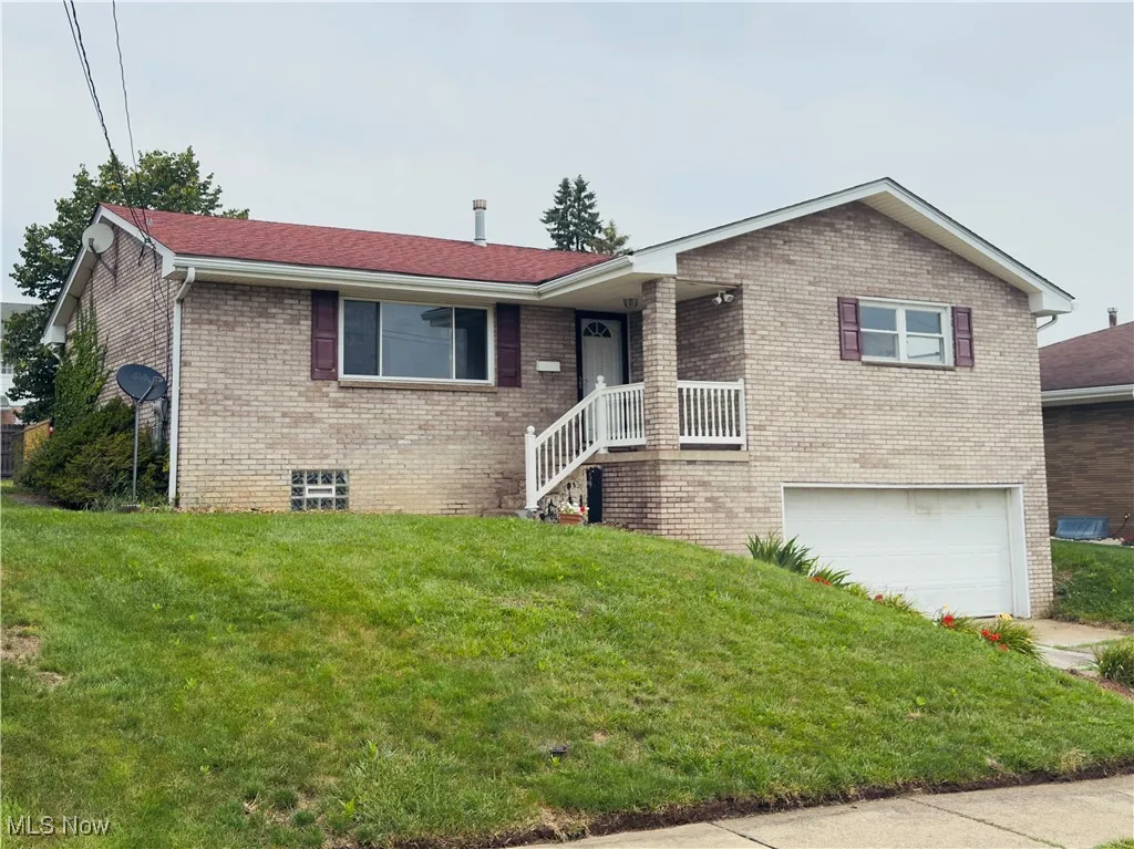 View of front of property featuring an attached garage, brick siding, a front lawn, and roof with shingles