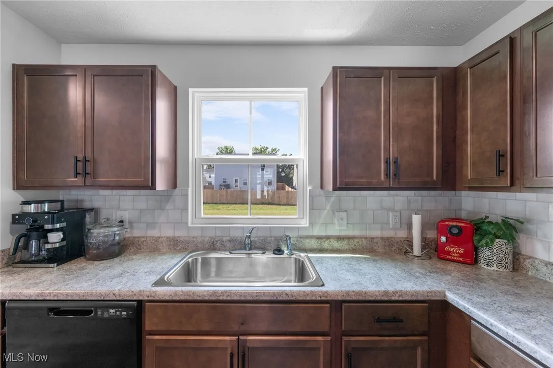 Kitchen with black dishwasher, light countertops, tasteful backsplash, and dark brown cabinetry