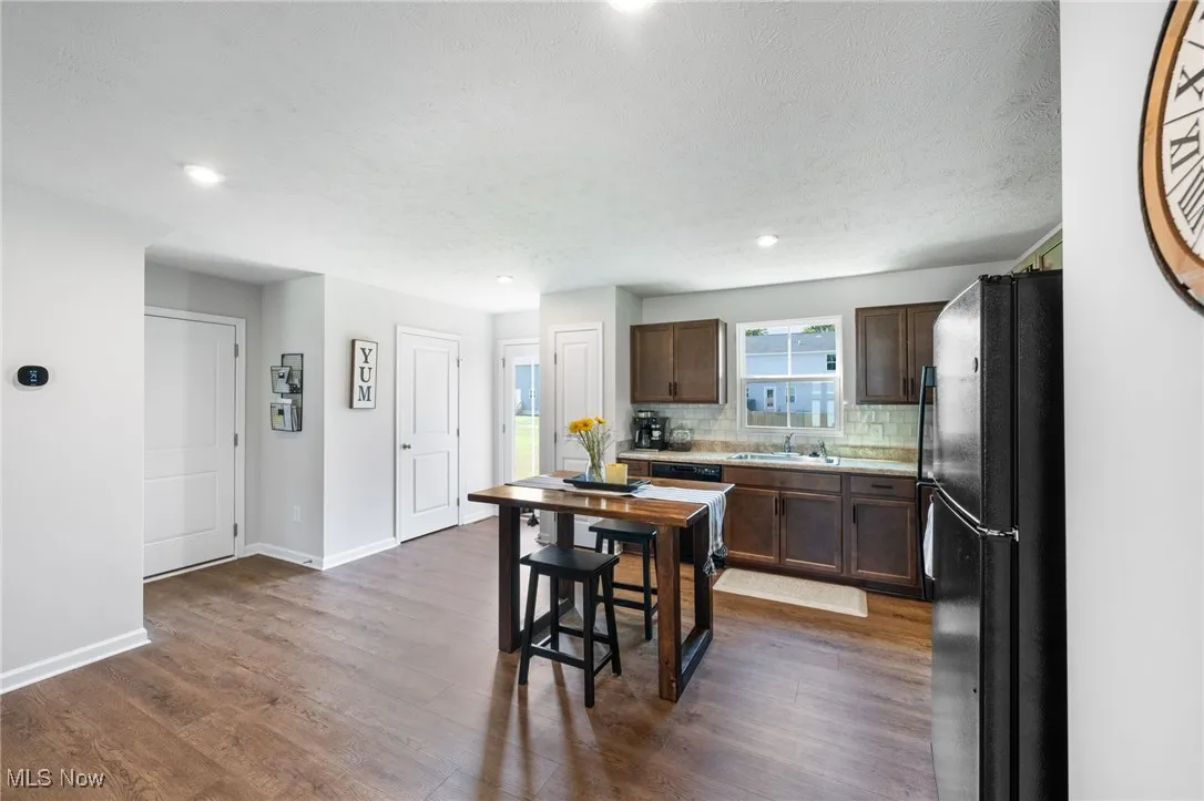 Kitchen featuring freestanding refrigerator, light countertops, tasteful backsplash, dark wood-style floors, and dark brown cabinetry