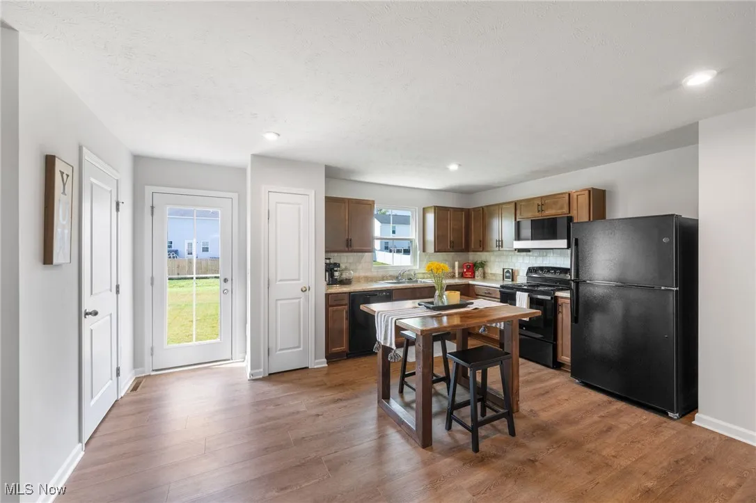 Kitchen with black appliances, backsplash, wood finished floors, light countertops, and recessed lighting
