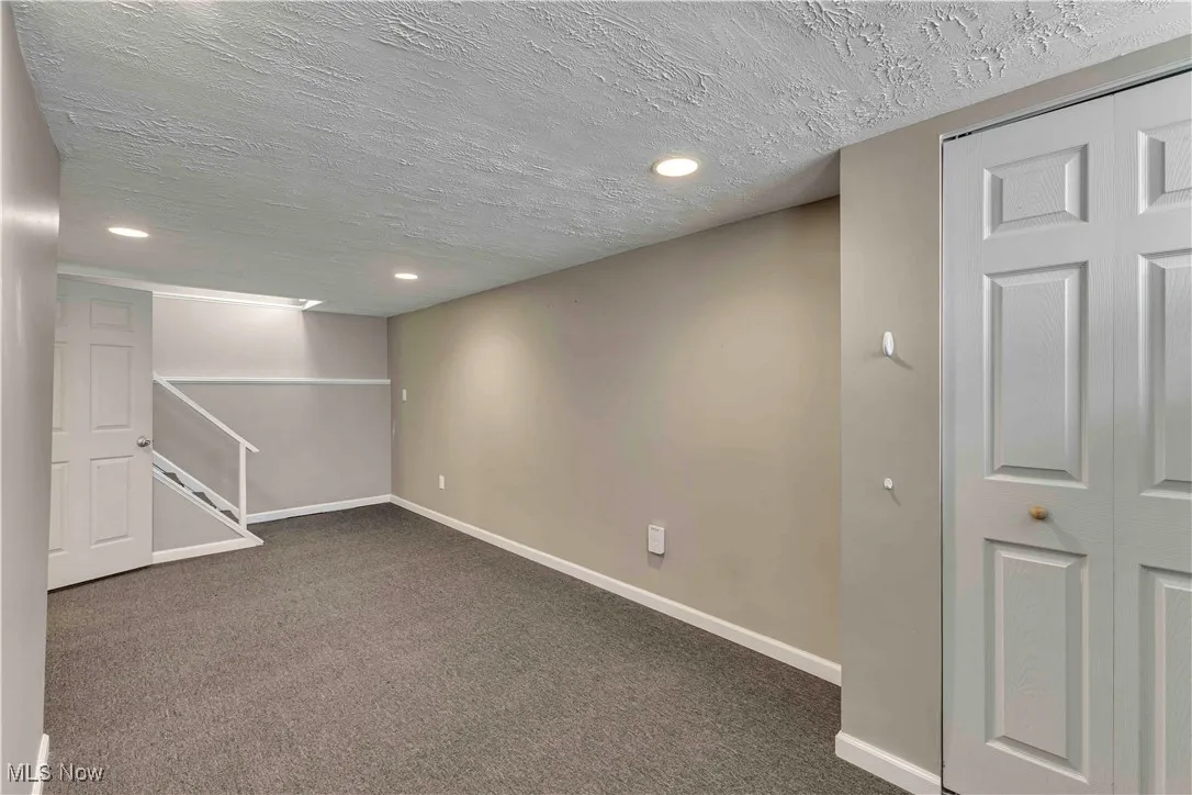 Finished below grade area with a textured ceiling, carpet, recessed lighting, and stairway