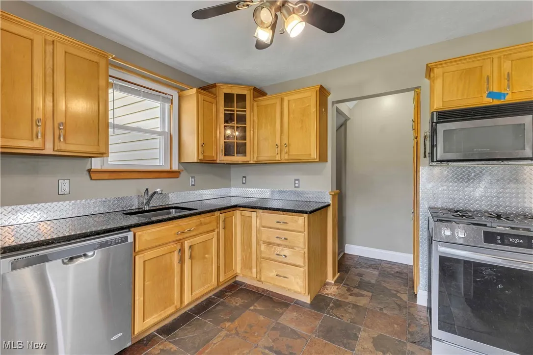 Kitchen featuring stainless steel appliances, a ceiling fan, glass insert cabinets, dark stone finish floors, and backsplash