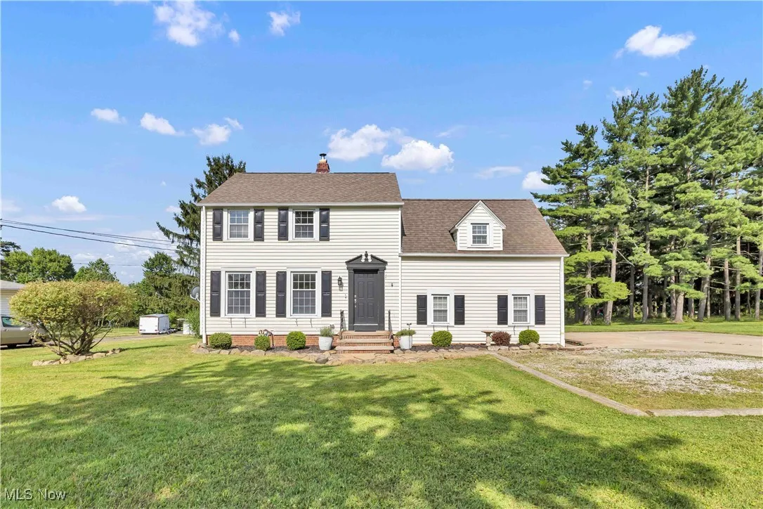 Colonial-style house featuring a front yard, a shingled roof, and a chimney