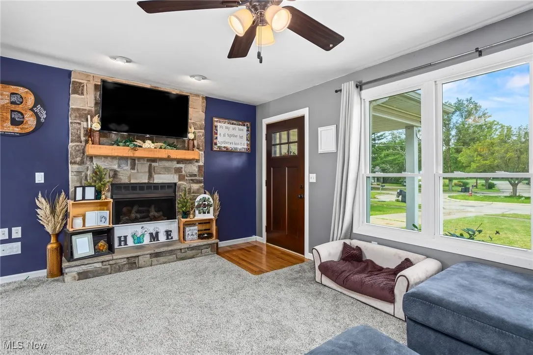 Carpeted living room featuring a fireplace and ceiling fan