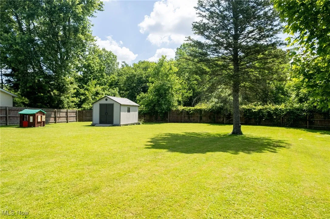 Fenced backyard featuring a storage shed, a playground, and view of wooded area