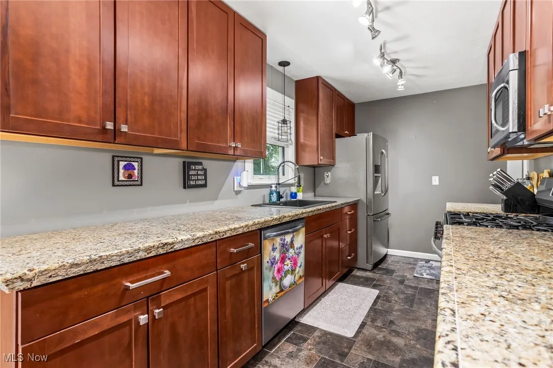 Kitchen with stainless steel appliances, stone finish flooring, light stone counters, and hanging light fixtures
