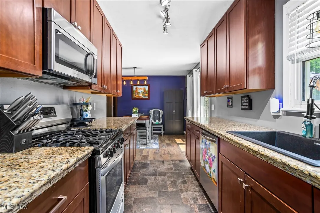 Kitchen featuring stainless steel appliances, stone finish flooring, light stone countertops, and reddish brown cabinets