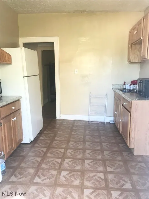 Kitchen with freestanding refrigerator, black microwave, and light floors