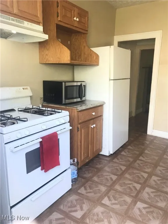 Kitchen featuring white appliances, under cabinet range hood, and brown cabinets