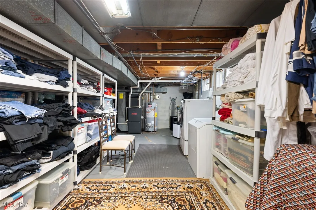 Unfinished below grade area with water heater, heating unit, and washer and clothes dryer