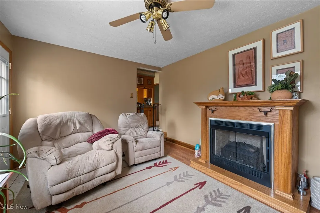 Living room with wood finished floors, ceiling fan, a fireplace, and a textured ceiling