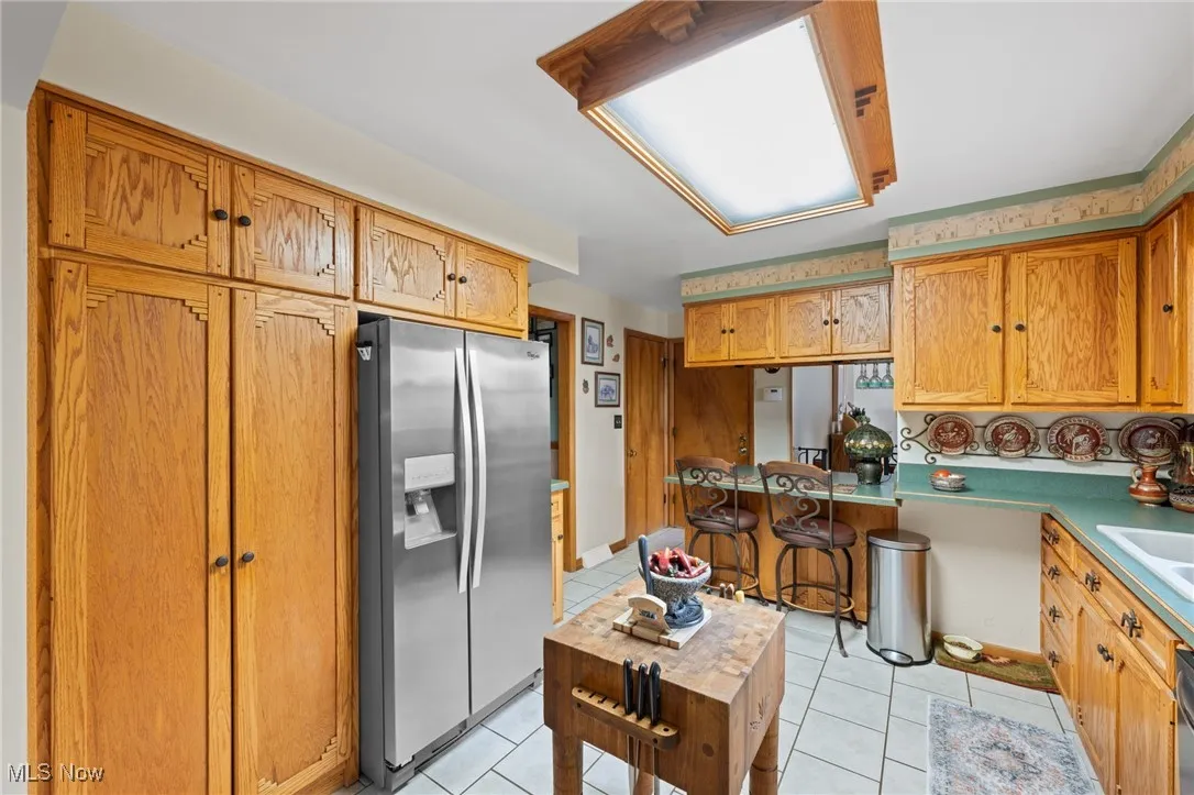 Kitchen with stainless steel refrigerator with ice dispenser, light tile patterned floors, and brown cabinets