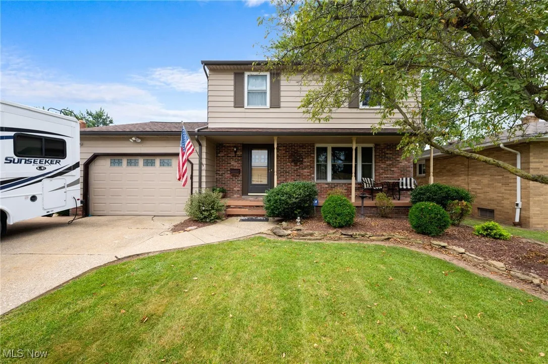 Traditional-style house with an attached garage, covered porch, concrete driveway, brick siding, and a front lawn