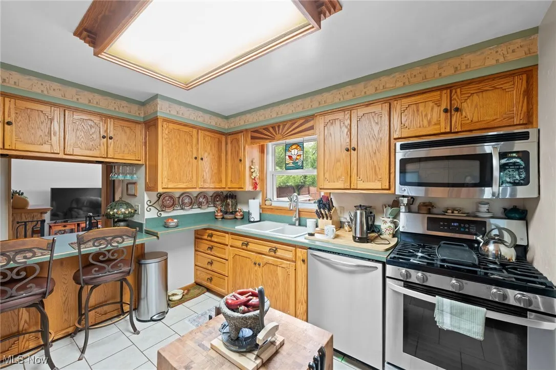 Kitchen with stainless steel appliances, light tile patterned flooring, light countertops, and brown cabinetry