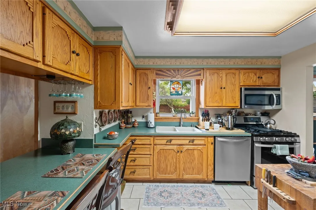 Kitchen featuring appliances with stainless steel finishes, light tile patterned flooring, light countertops, and brown cabinets