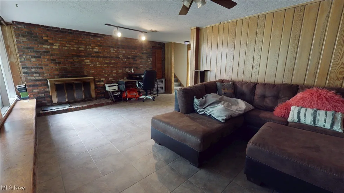 Basement Living area featuring wooden walls, stairway, a ceiling fan, a textured ceiling, and a brick fireplace
