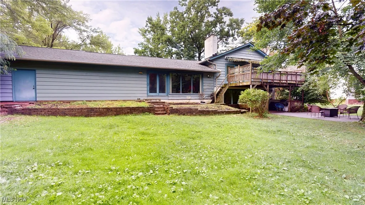 Rear view of house with a deck, a chimney, a lawn, and a patio