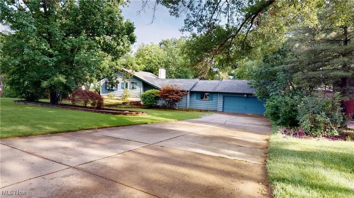 Ranch-style house with a chimney, concrete driveway, a garage, and a front lawn