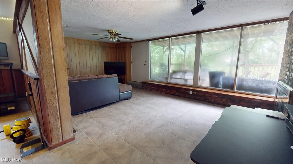 Basement Living area featuring a ceiling fan, a textured ceiling, and wooden walls