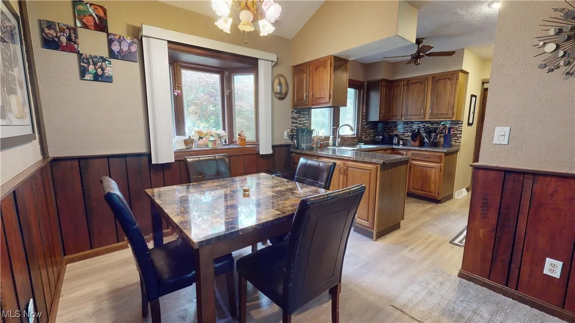 Dining space featuring light wood-type flooring, ceiling fan, wainscoting, a chandelier, and lofted ceiling