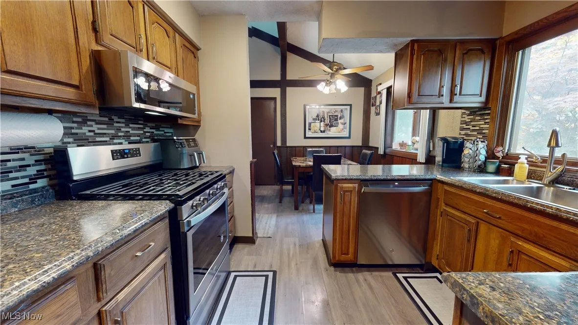Kitchen with appliances with stainless steel finishes, light wood-type flooring, backsplash, ceiling fan, and lofted ceiling