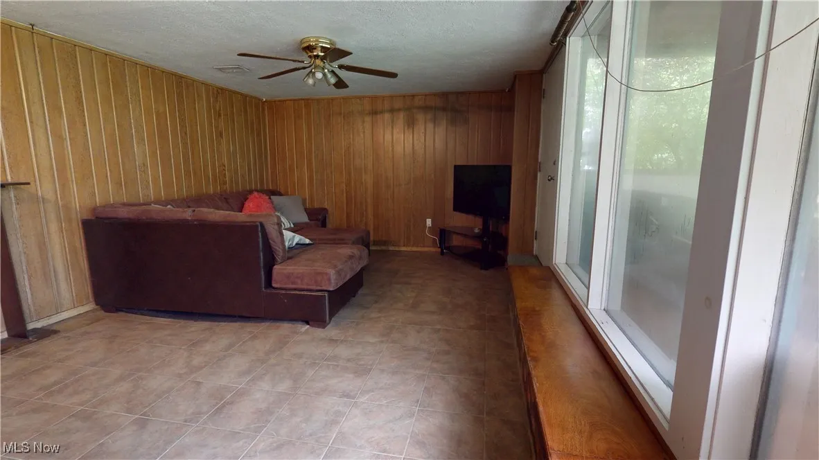 Basement Living room featuring a ceiling fan, wood walls, and a textured ceiling