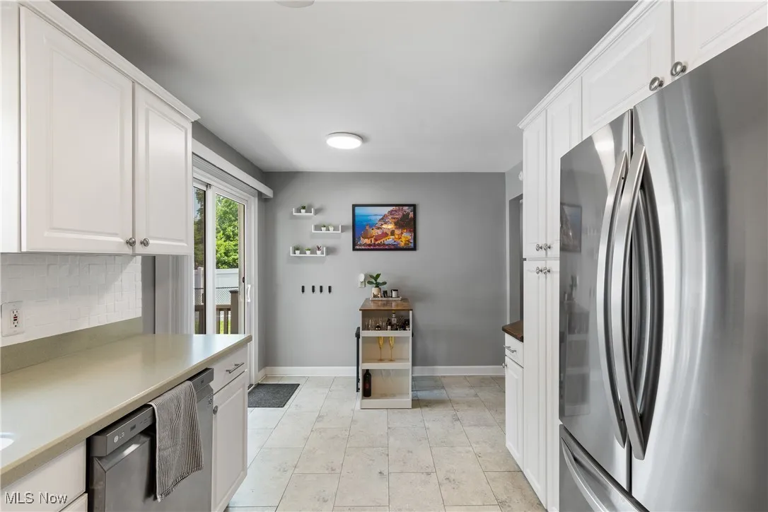 Kitchen with freestanding refrigerator, backsplash, white cabinets, dishwasher, and light countertops