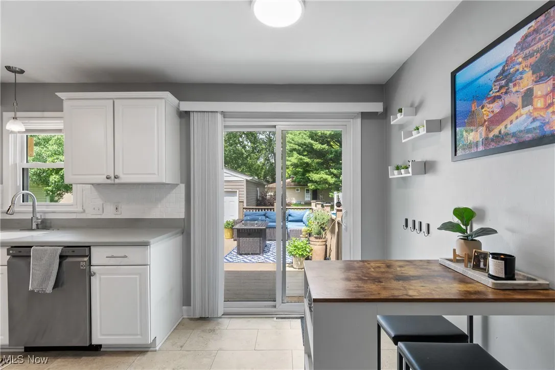 Kitchen with stainless steel dishwasher, white cabinets, and plenty of natural light