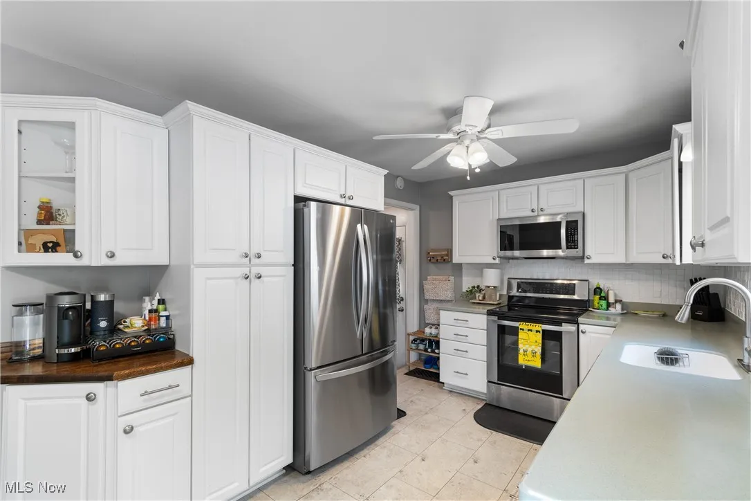 Kitchen with appliances with stainless steel finishes, white cabinets, ceiling fan, and decorative backsplash