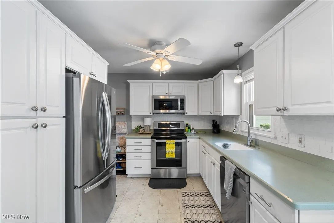 Kitchen featuring appliances with stainless steel finishes, tasteful backsplash, white cabinetry, and ceiling fan