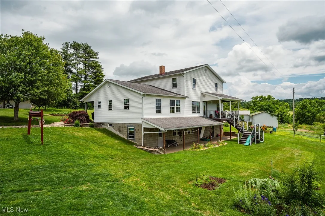 Rear view of property with a patio area, a shingled roof, stairs, and a lawn