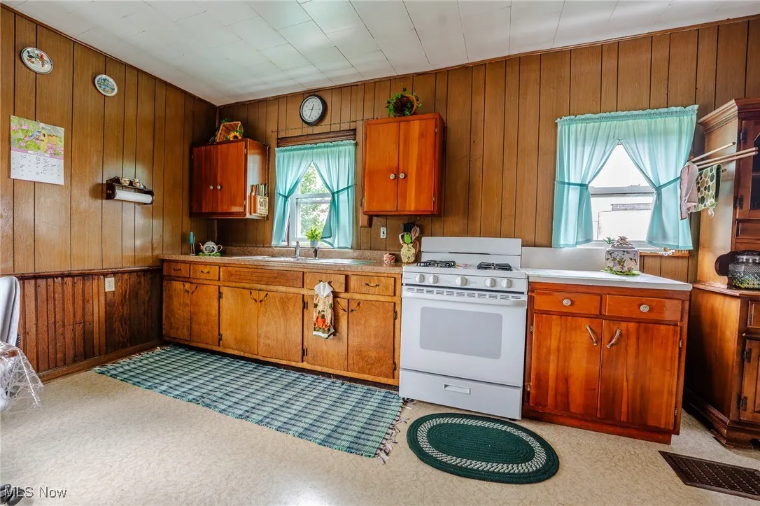 Kitchen featuring gas range gas stove, brown cabinetry, wooden walls, and light countertops