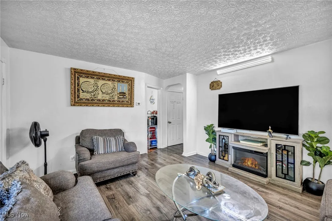 Living area with wood finished floors, a glass covered fireplace, arched walkways, and an ornate ceiling