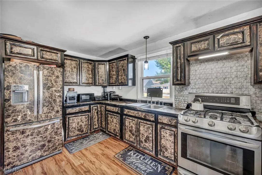 Kitchen with stainless steel gas range, fridge with ice dispenser, dark countertops, dark brown cabinets, and light wood-style floors