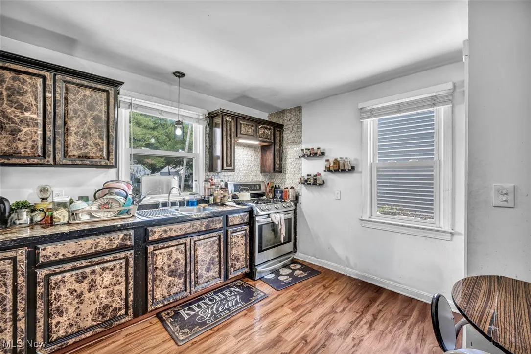 Kitchen with stainless steel range with gas stovetop, light wood-style flooring, dark countertops, dark brown cabinetry, and pendant lighting