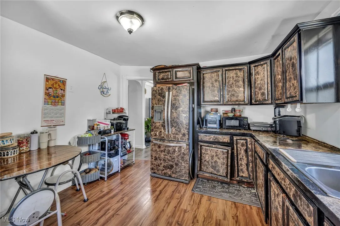 Kitchen with refrigerator with ice dispenser, black microwave, light wood finished floors, dark countertops, and dark brown cabinets