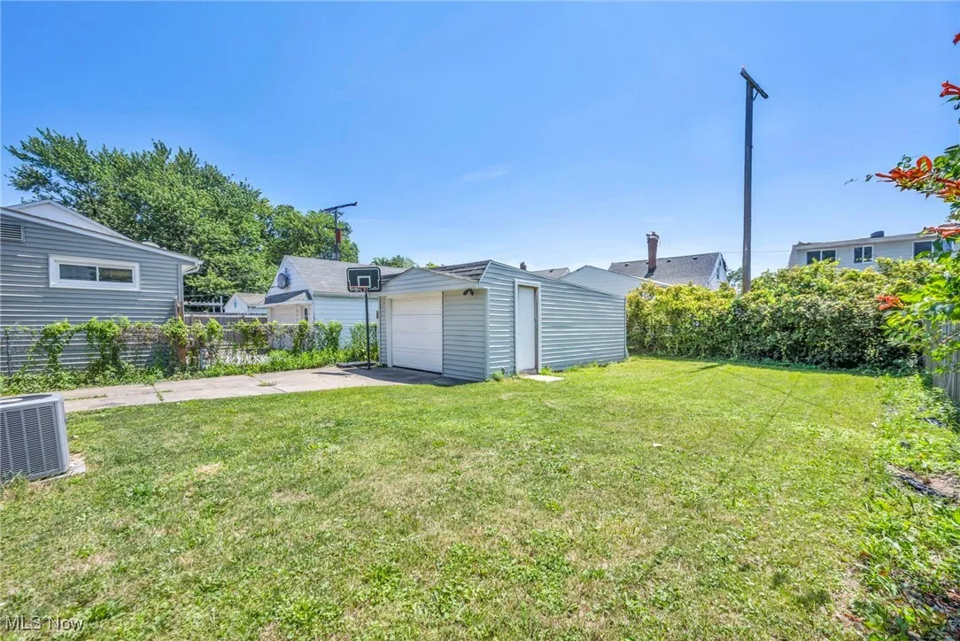 View of green lawn with an outdoor structure, a detached garage, and driveway
