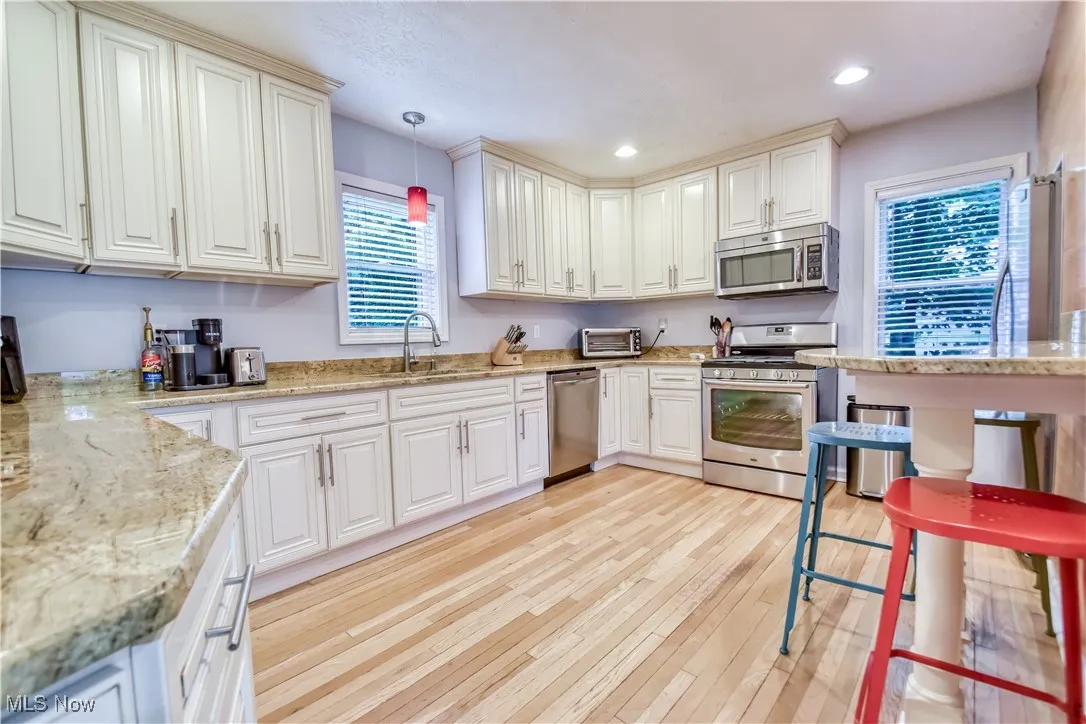 Kitchen with stainless steel appliances, light wood-style floors, hanging light fixtures, recessed lighting, and white cabinets