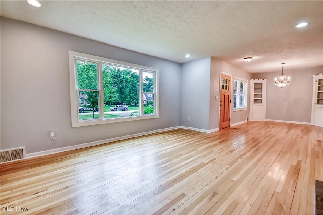 Unfurnished living room featuring a chandelier, light wood-type flooring, a textured ceiling, and recessed lighting